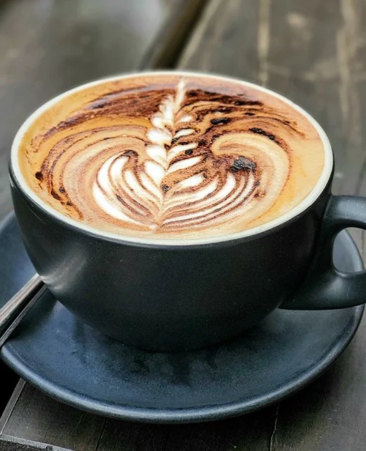 A flat white with latte art in a black cup at Goodness Coffee Co.