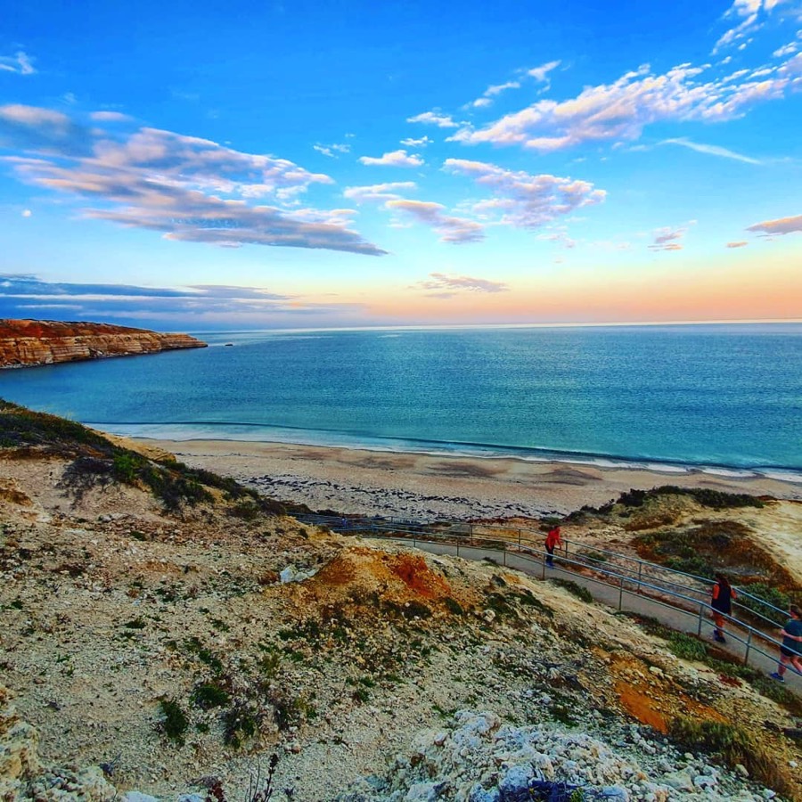 Ochre cliffs and turquoise water at Port Willunga Beach at sunset, with the boardwalk winding down to the sand