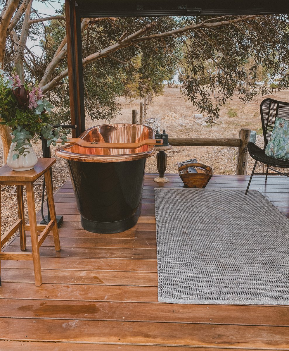 The copper bath under the pergola, a rug, stool and chair beside it