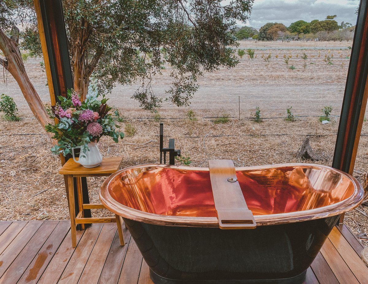 The copper bath on the deck with a jug of flowers, paddocks beyond