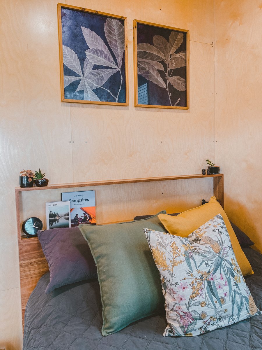 Cushions on the queen bed against warm timber walls, botanical prints above