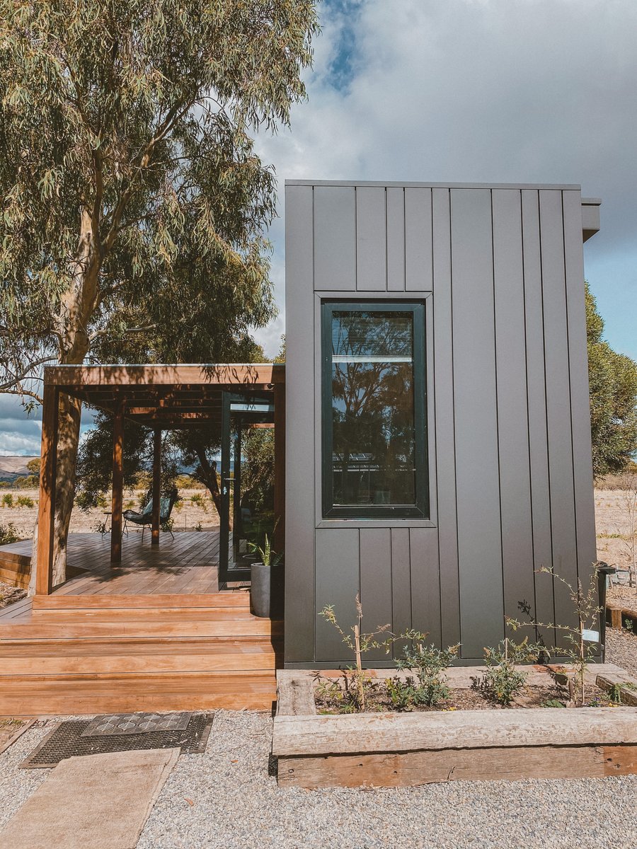 The cabin's black side wall beside the timber deck, gums behind
