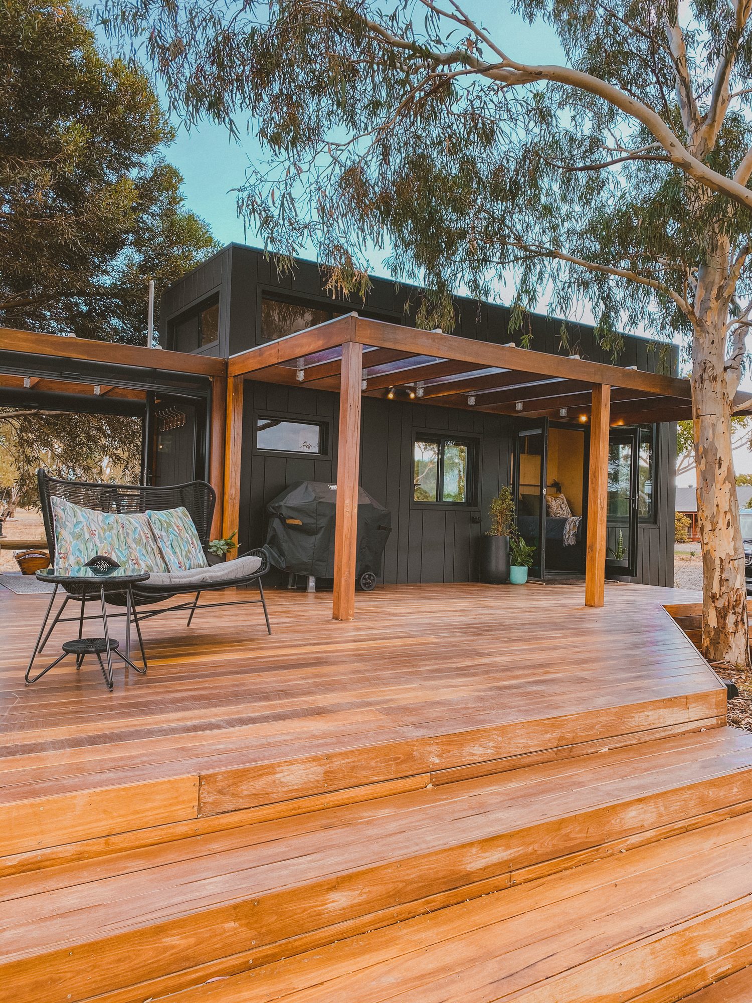 The cabin's wide timber deck and pergola, an outdoor sofa and barbecue, gum trees above
