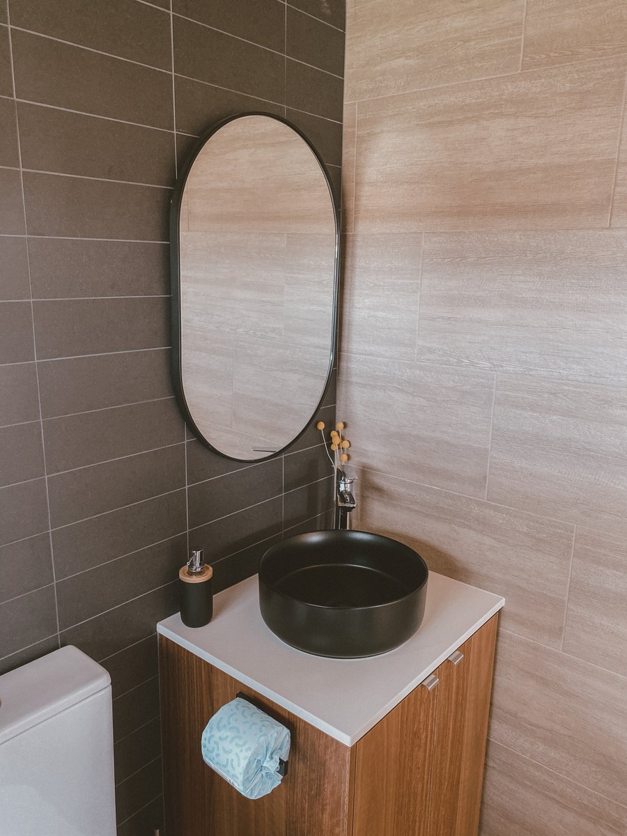 The vanity: a black basin, oval mirror and timber walls