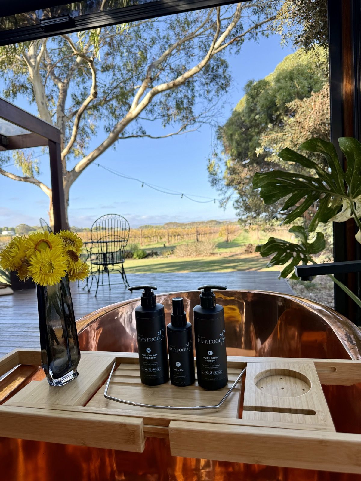 Hair Food shampoo and conditioner on the bath caddy across the copper bath, the deck and vineyard beyond